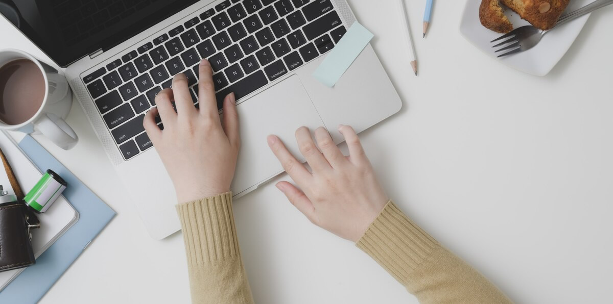 Overhead shot of young female typing on laptop computer in comfortable workspace